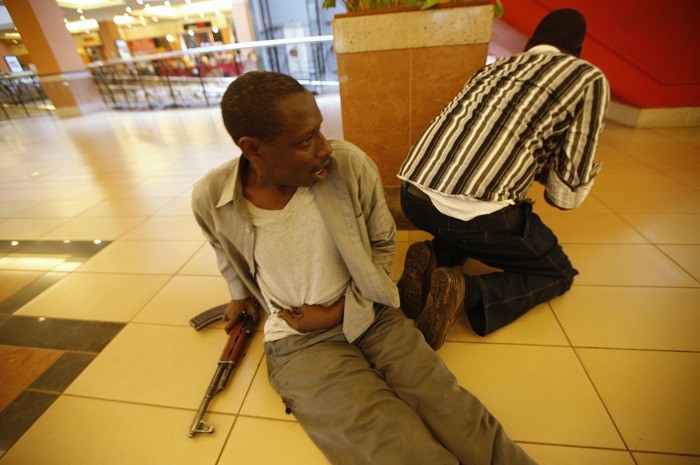 An injured policeman holds on to his wound as his compatriot searches through the Westgate shopping centre for gunmen in Nairobi